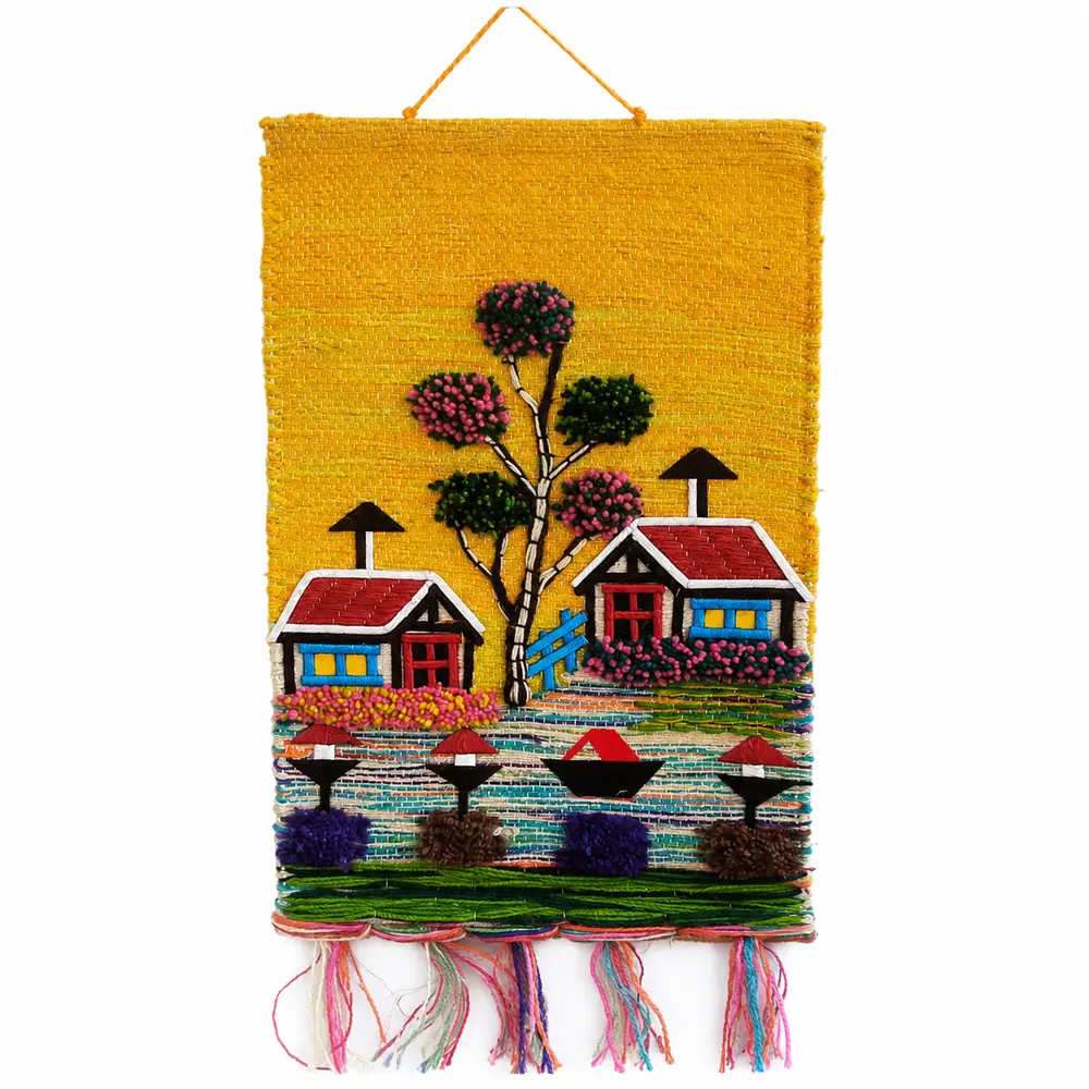 Handmade woven jute wall hanging with an embroidered village scene of two cottages, a tree, boats and colourful fringe on a yellow background