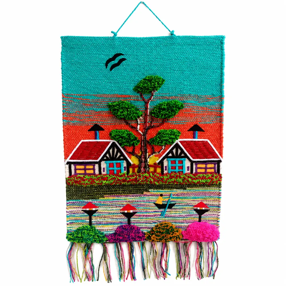 Woven wall hanging with a turquoise and orange sunset sky, two red-roofed cottages either side of a green tree, a boat and bright tufted bushes