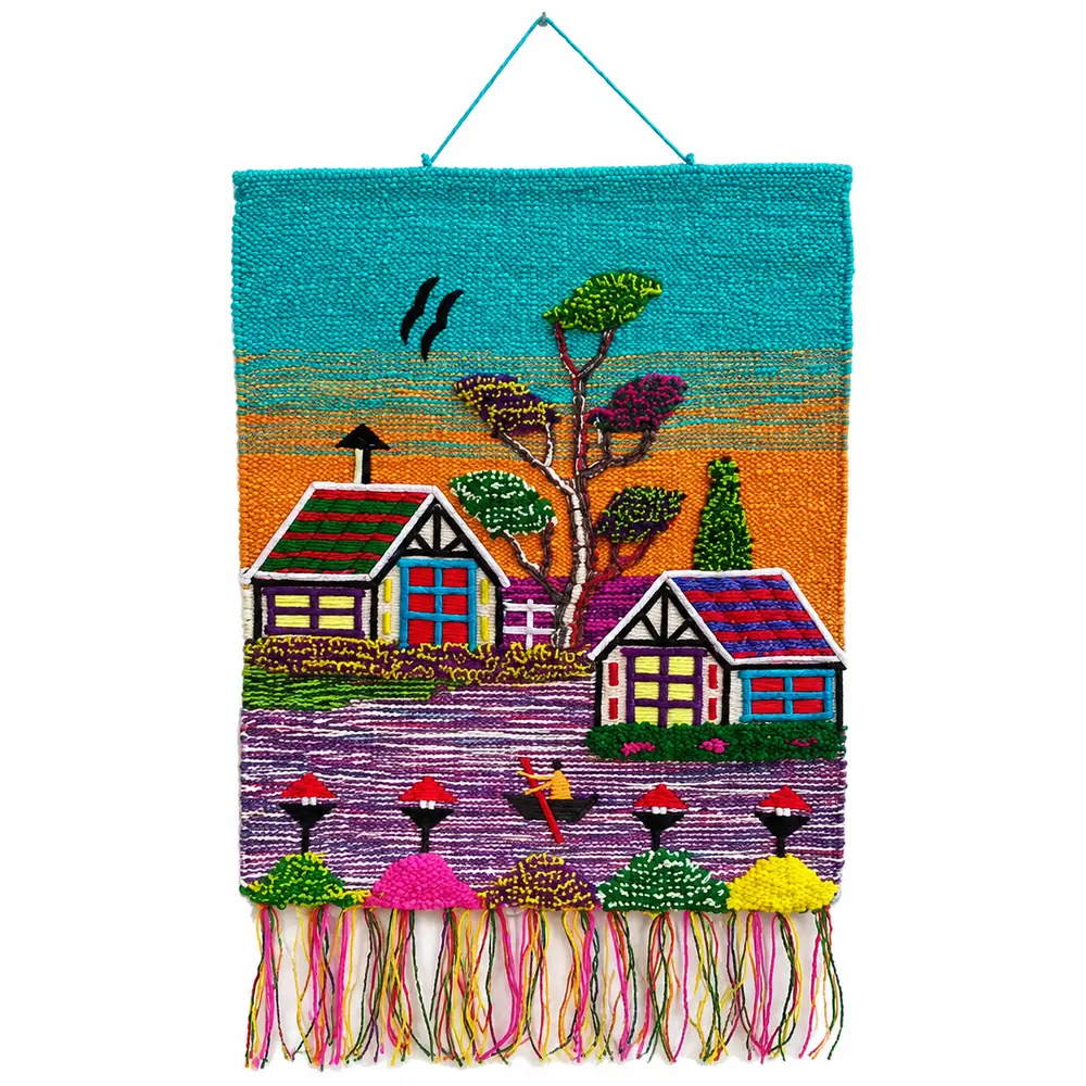 Handmade woven wall hanging with turquoise and orange sky, two cottages by a purple lake, a rower in a boat and pink, green and yellow bushes